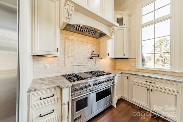 kitchen featuring dark hardwood / wood-style floors, decorative backsplash, custom exhaust hood, light stone counters, and stainless steel appliances