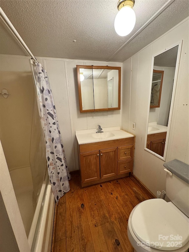 full bathroom featuring vanity, a textured ceiling, shower / tub combo with curtain, hardwood / wood-style floors, and toilet