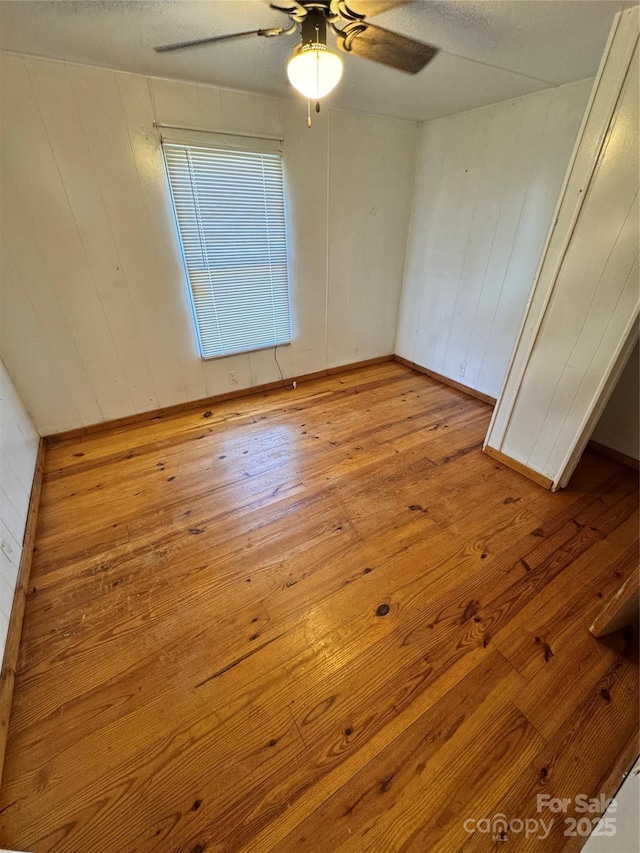 unfurnished room featuring ceiling fan, light hardwood / wood-style flooring, wood walls, and a textured ceiling