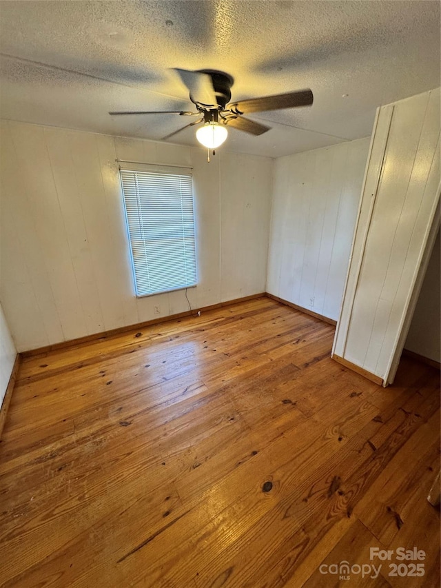 empty room with ceiling fan, wood walls, light wood-type flooring, and a textured ceiling