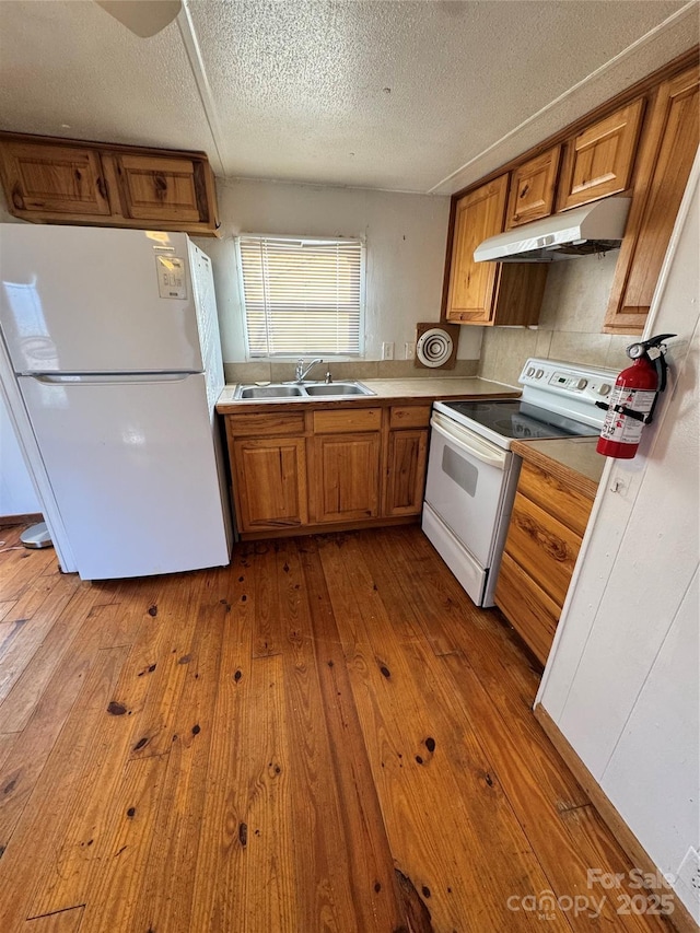 kitchen featuring a textured ceiling, white appliances, light hardwood / wood-style flooring, and sink