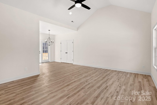 spare room featuring ceiling fan with notable chandelier, high vaulted ceiling, light wood-style flooring, and baseboards