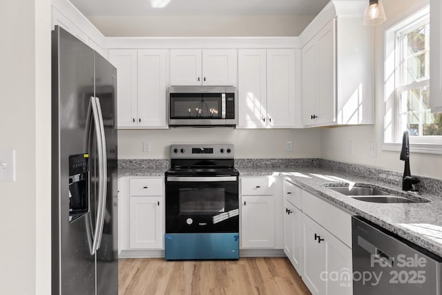 kitchen with light wood-style flooring, stainless steel appliances, a sink, white cabinets, and light stone countertops