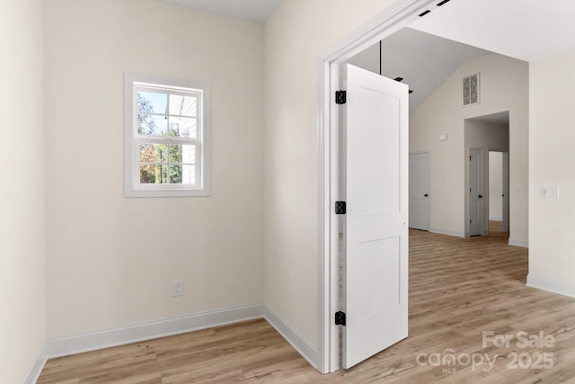 empty room with lofted ceiling, light wood-style flooring, visible vents, and baseboards