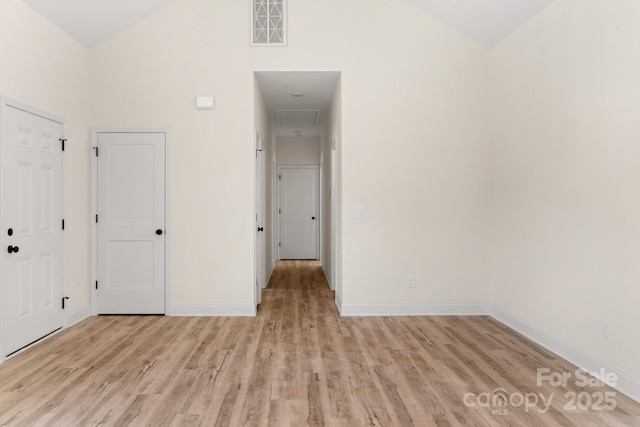 empty room with high vaulted ceiling, light wood-type flooring, visible vents, and baseboards