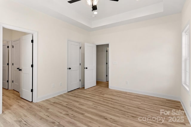 unfurnished bedroom with baseboards, ceiling fan, a raised ceiling, and light wood-style floors