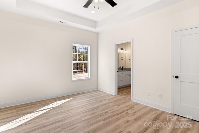 unfurnished bedroom with visible vents, baseboards, connected bathroom, a tray ceiling, and light wood-type flooring