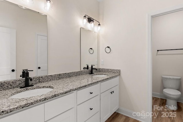 full bathroom with double vanity, baseboards, a sink, and wood finished floors