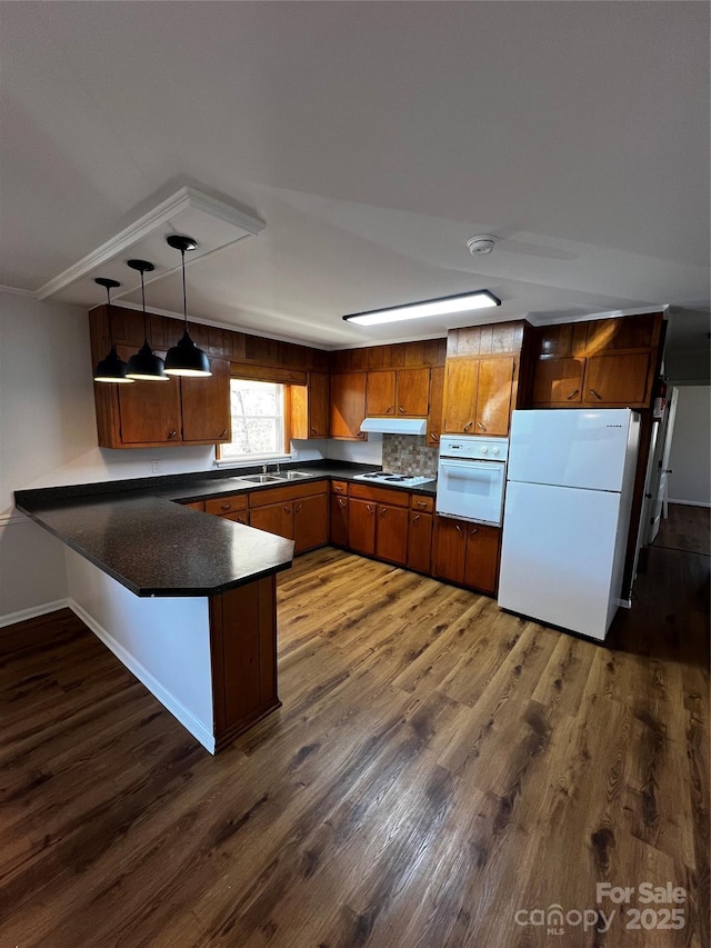 kitchen with kitchen peninsula, white appliances, dark wood-type flooring, sink, and pendant lighting