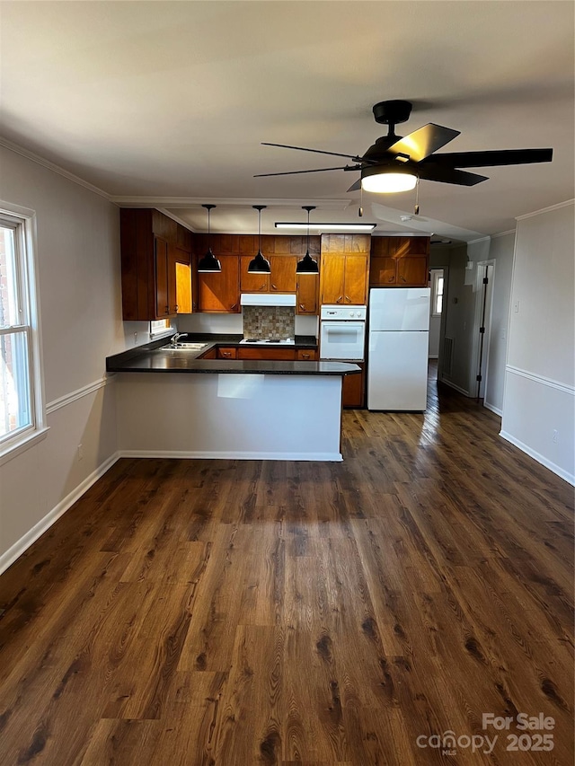 kitchen featuring kitchen peninsula, decorative backsplash, white appliances, dark wood-type flooring, and decorative light fixtures