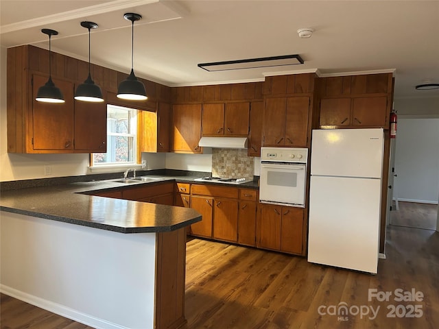 kitchen with sink, dark wood-type flooring, kitchen peninsula, pendant lighting, and white appliances