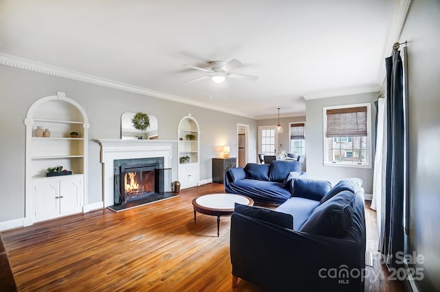 living room featuring built in shelves, ceiling fan, ornamental molding, and hardwood / wood-style flooring