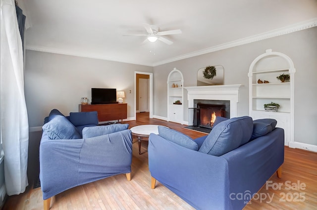 living room featuring hardwood / wood-style floors, built in shelves, ceiling fan, and crown molding