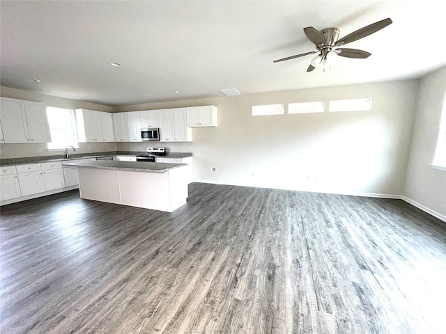 kitchen with stainless steel appliances, a sink, a kitchen island, white cabinetry, and dark wood finished floors