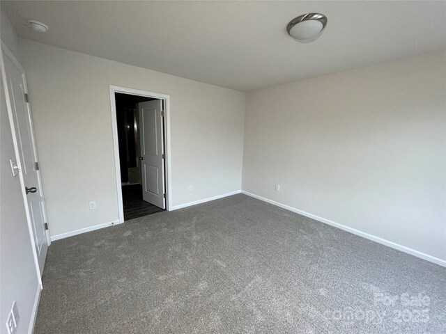 unfurnished room featuring dark colored carpet and baseboards