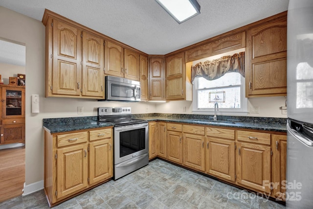 kitchen featuring dark stone countertops, sink, a textured ceiling, and appliances with stainless steel finishes