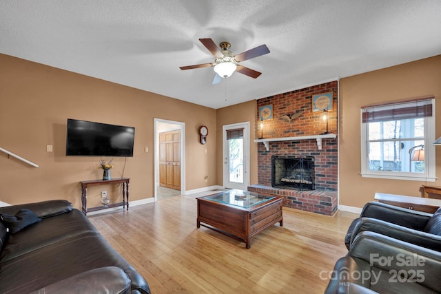 living room with ceiling fan, a fireplace, a textured ceiling, and light wood-type flooring