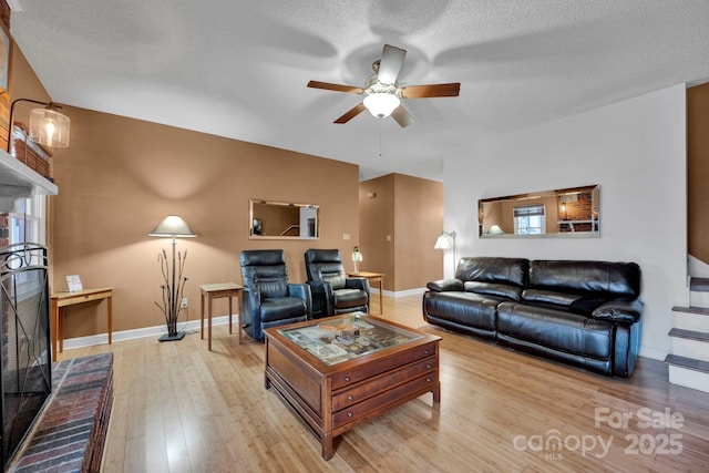 living room with ceiling fan, light hardwood / wood-style flooring, a textured ceiling, and a brick fireplace