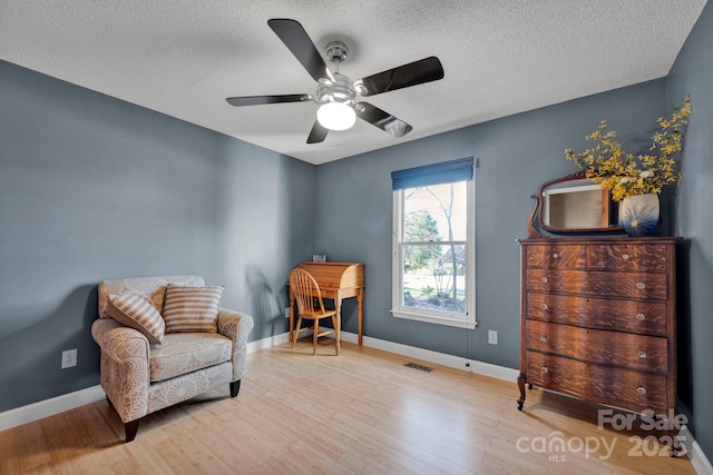 living area with ceiling fan, light wood-type flooring, and a textured ceiling