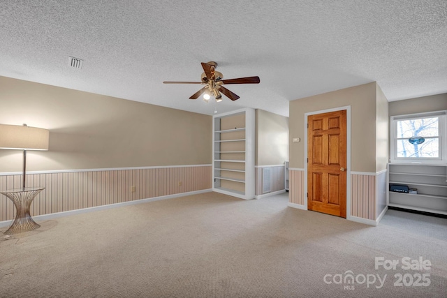 additional living space with ceiling fan, light colored carpet, built in features, and a textured ceiling