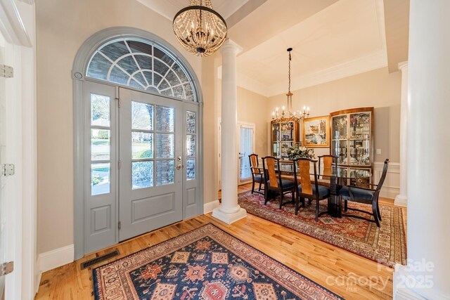 entrance foyer with decorative columns, ornamental molding, a chandelier, and hardwood / wood-style flooring