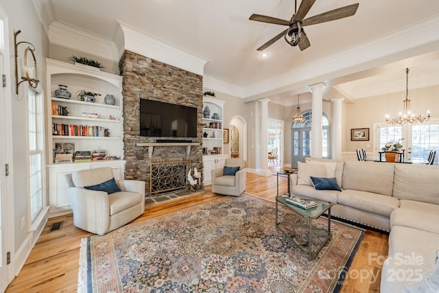 living room with built in features, ceiling fan with notable chandelier, light hardwood / wood-style flooring, and a stone fireplace