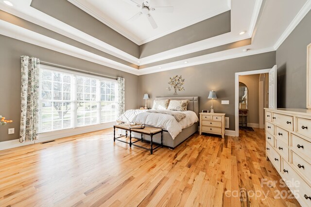 bedroom with a raised ceiling, ceiling fan, ornamental molding, and light wood-type flooring