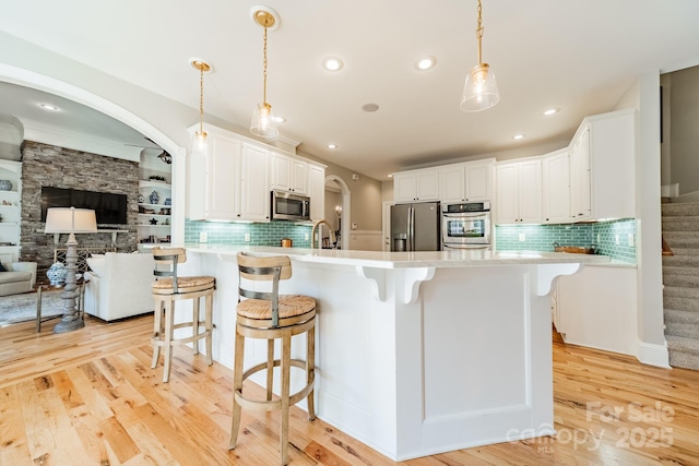 kitchen with a kitchen island with sink, white cabinetry, hanging light fixtures, and appliances with stainless steel finishes