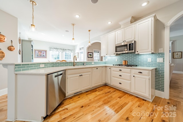 kitchen featuring kitchen peninsula, appliances with stainless steel finishes, sink, white cabinetry, and hanging light fixtures