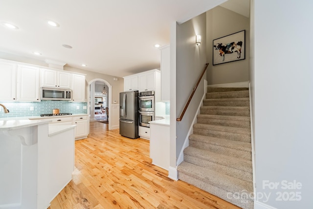 kitchen featuring decorative backsplash, white cabinets, stainless steel appliances, and light hardwood / wood-style floors