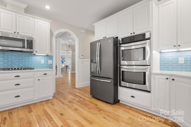 4150 Summit Ridge Ln, Denver, NC 28037 - kitchen featuring appliances with stainless steel finishes, arched walkways, light countertops, backsplash, and white cabinets