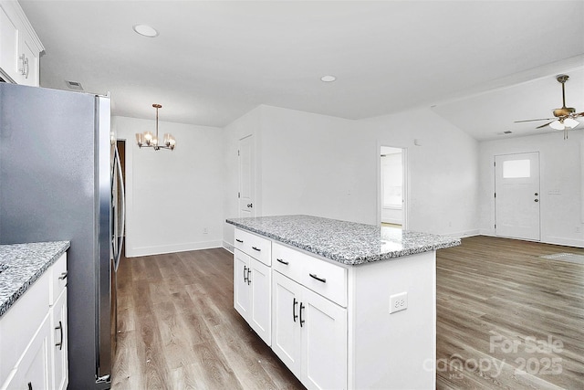 kitchen featuring ceiling fan with notable chandelier, light stone countertops, a center island, white cabinetry, and stainless steel fridge