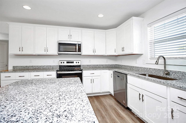 kitchen with sink, light stone countertops, white cabinets, and appliances with stainless steel finishes