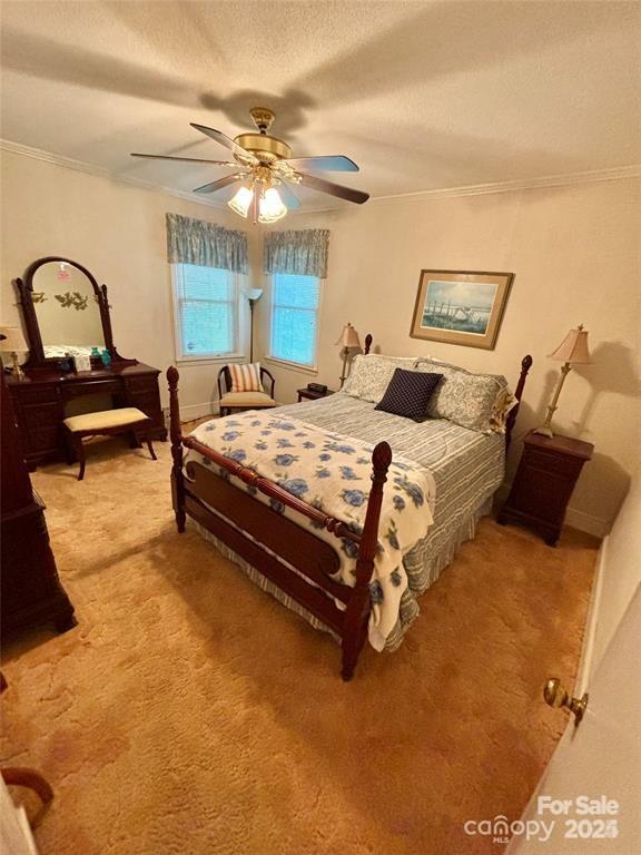 bedroom featuring a textured ceiling, carpet floors, ceiling fan, and ornamental molding