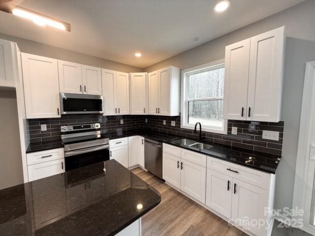 kitchen with white cabinets, sink, dark stone countertops, light hardwood / wood-style floors, and stainless steel appliances