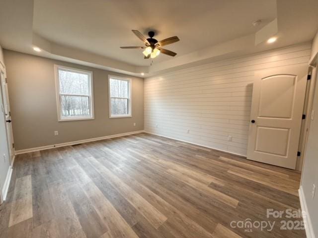 spare room with ceiling fan, a raised ceiling, and wood-type flooring