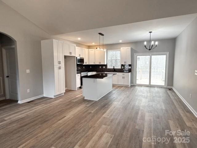 kitchen with white cabinets, decorative light fixtures, a kitchen island, and backsplash