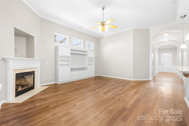 unfurnished living room featuring hardwood / wood-style flooring, ceiling fan, ornamental molding, and a high end fireplace