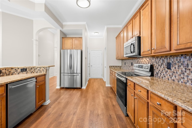 kitchen with crown molding, light hardwood / wood-style flooring, appliances with stainless steel finishes, light stone countertops, and decorative backsplash