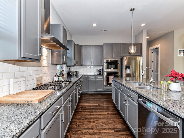 kitchen featuring appliances with stainless steel finishes, gray cabinetry, wall chimney exhaust hood, sink, and decorative light fixtures