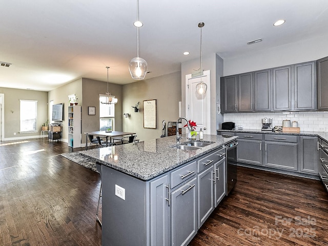 kitchen with sink, dark stone countertops, decorative light fixtures, decorative backsplash, and a center island with sink