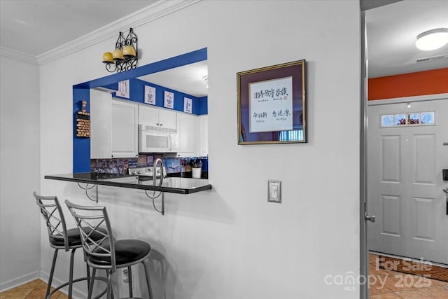 kitchen featuring a kitchen bar, backsplash, white cabinets, and light tile patterned flooring