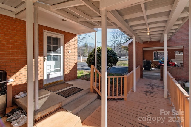 exterior space with beam ceiling, light hardwood / wood-style floors, and brick wall