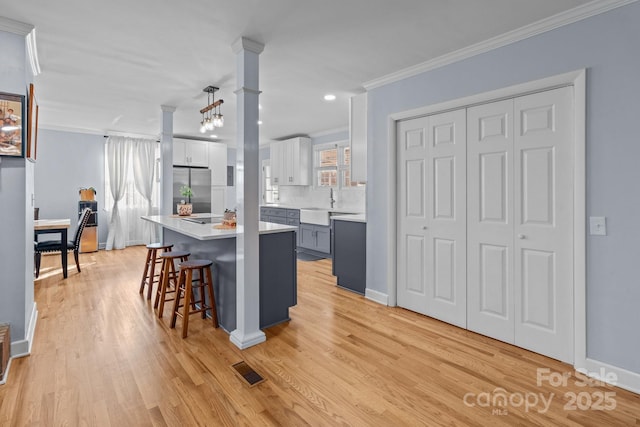 kitchen featuring ornamental molding, gray cabinetry, a breakfast bar, stainless steel refrigerator, and hanging light fixtures