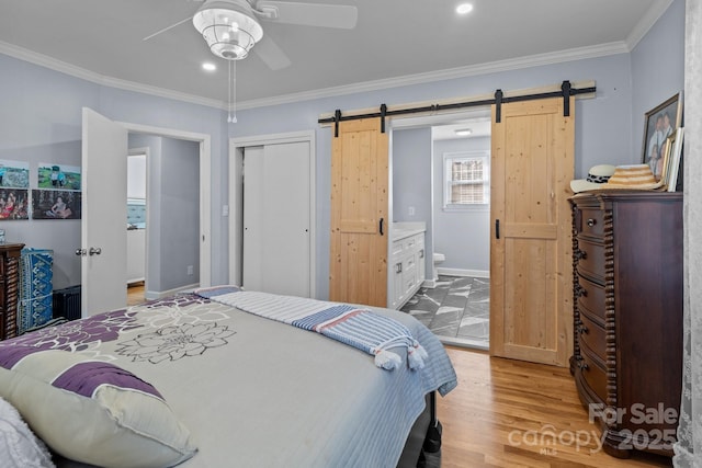 bedroom with ceiling fan, a barn door, ensuite bathroom, crown molding, and a closet