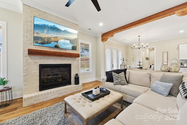 living room featuring ceiling fan with notable chandelier, crown molding, a fireplace, and light hardwood / wood-style flooring