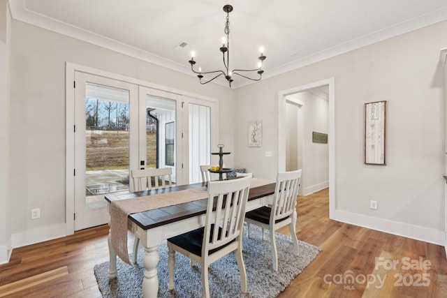 dining space featuring wood-type flooring, ornamental molding, and an inviting chandelier