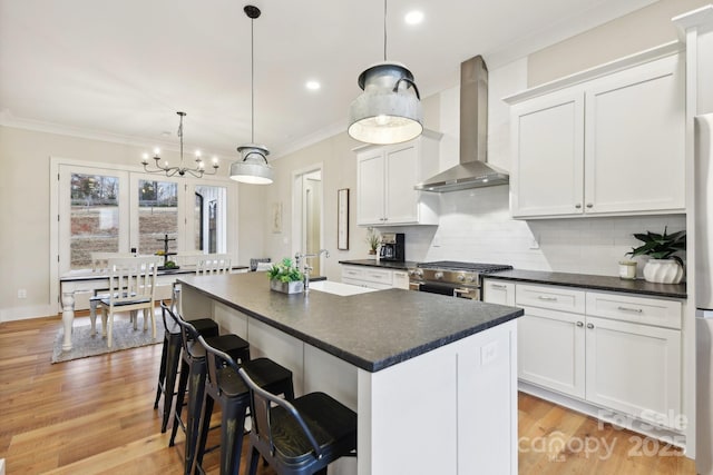 kitchen featuring a center island, white cabinetry, hanging light fixtures, appliances with stainless steel finishes, and wall chimney exhaust hood