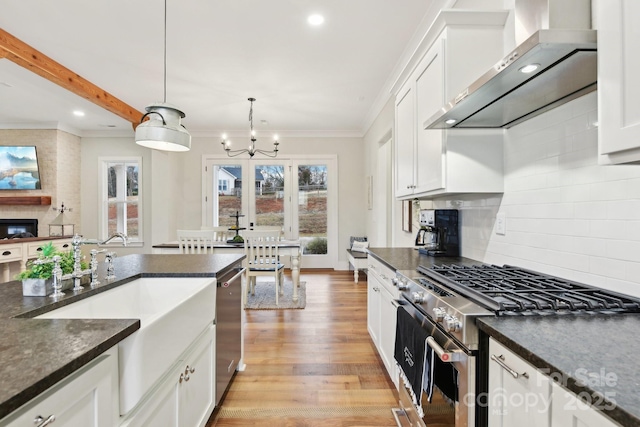 kitchen featuring decorative light fixtures, appliances with stainless steel finishes, wall chimney exhaust hood, and white cabinetry