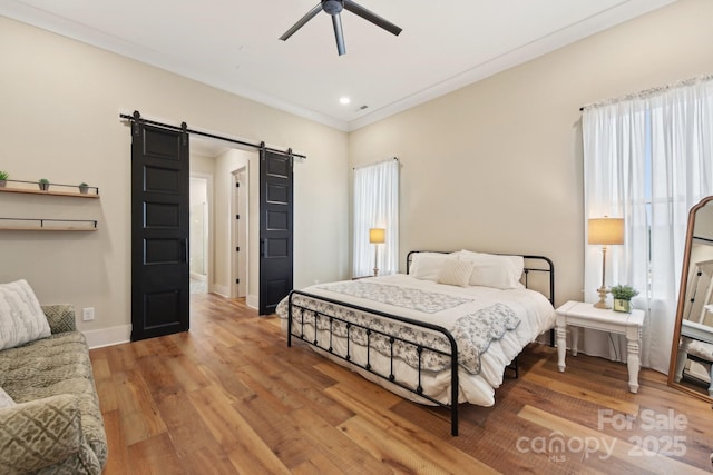 bedroom with hardwood / wood-style floors, multiple windows, ceiling fan, crown molding, and a barn door